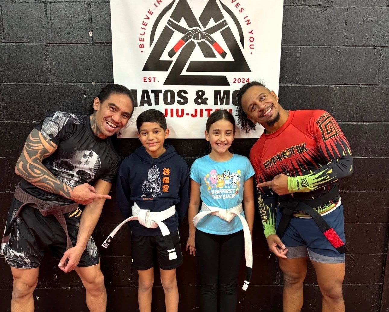 Two kids with their coaches in front of the Matos & Mora banner